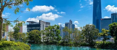 A modern building with a reflective glass facade, surrounded by lush greenery and a clear blue sky.
