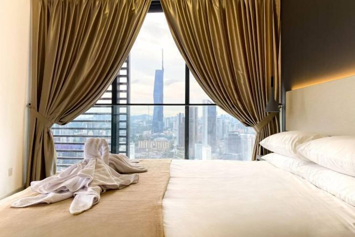 A hotel room with a large window, a bed, and a view of a city skyline.
