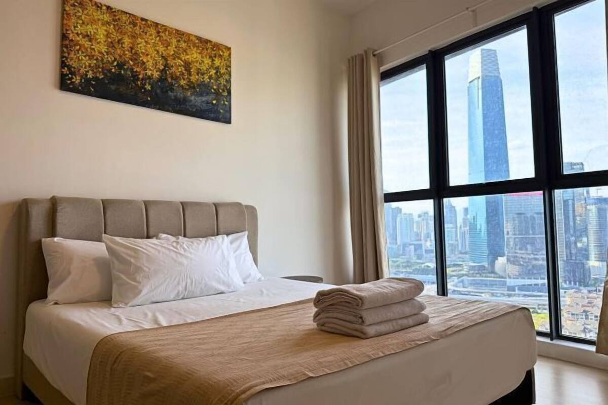 A hotel room with a large bed, a city view, and a painting on the wall.
