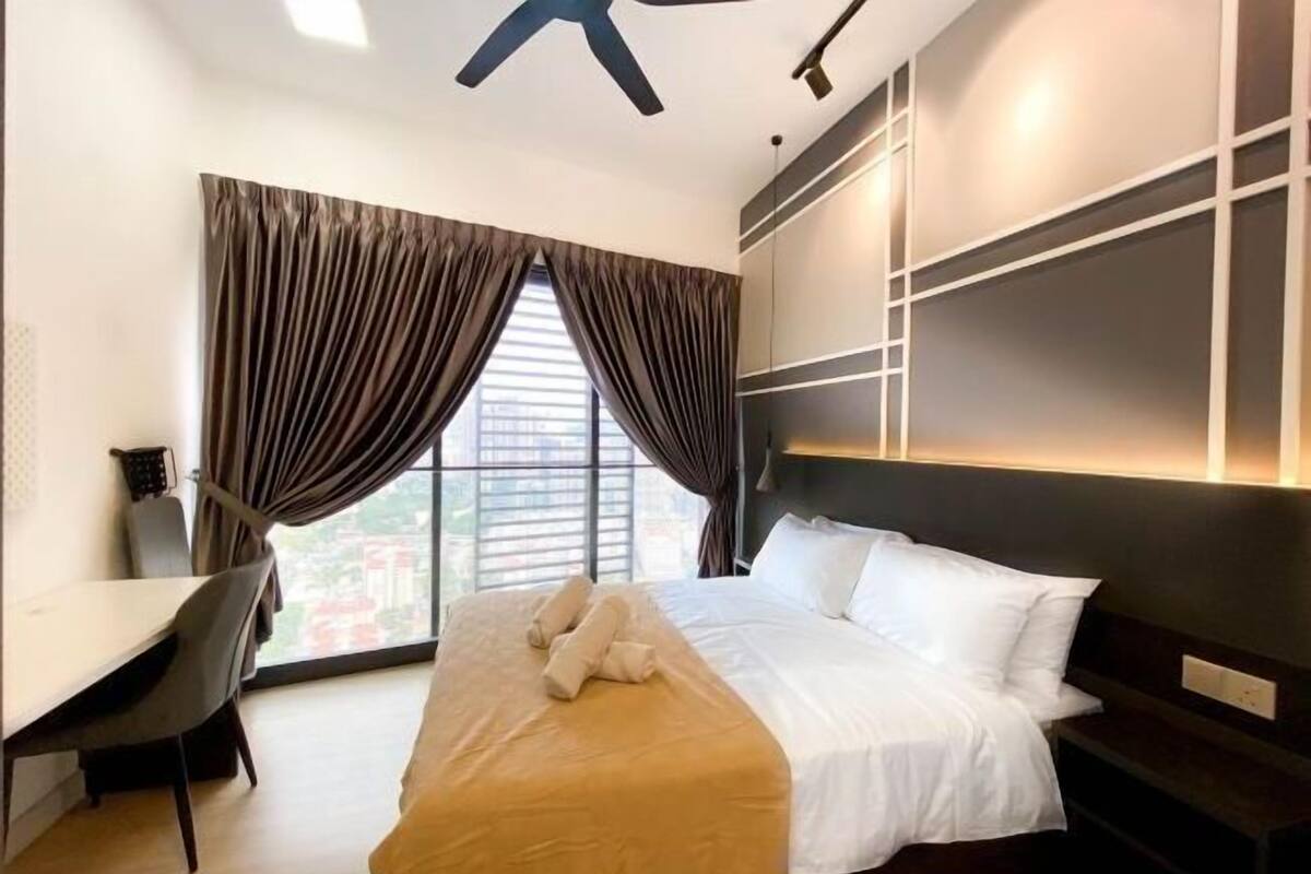 A hotel room with a bed, a desk, and a large window with curtains.