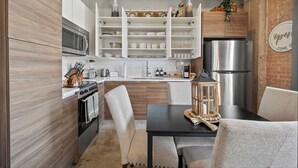 Una cocina compacta con armarios blancos, un refrigerador de acero inoxidable y un comedor con mesa y sillas.