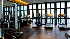 Ein Fitnessstudio mit Trainingsgeräten, großen Fenstern und Blick auf die Stadt.