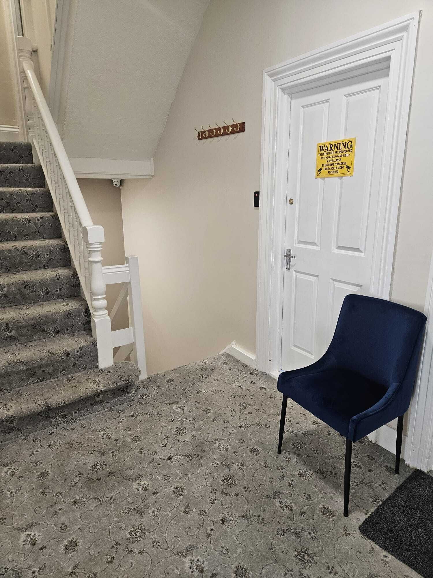 A staircase with a white handrail and a dark blue chair in a hallway with patterned carpet.