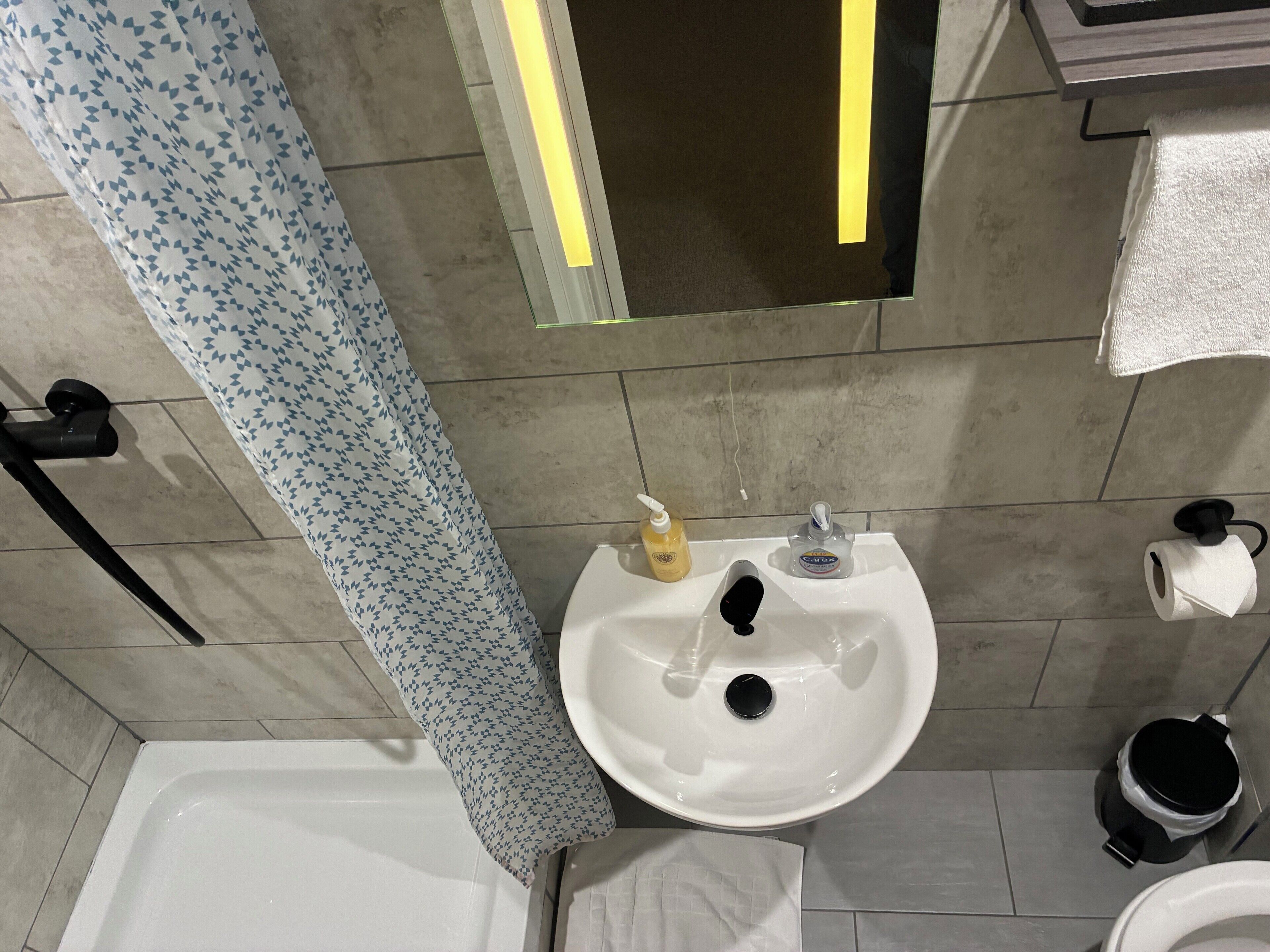 Un baño con lavamanos blanco, un espejo, una toalla, un inodoro y una cortina de ducha.