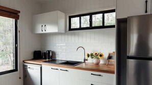 Una cocina moderna con armarios blancos, lavavajillas de acero inoxidable, un lavaplatos y un refrigerador.