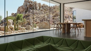Een modern interieur met een groene zithoek, een eettafel en uitzicht op een rotsachtig landschap door grote ramen.