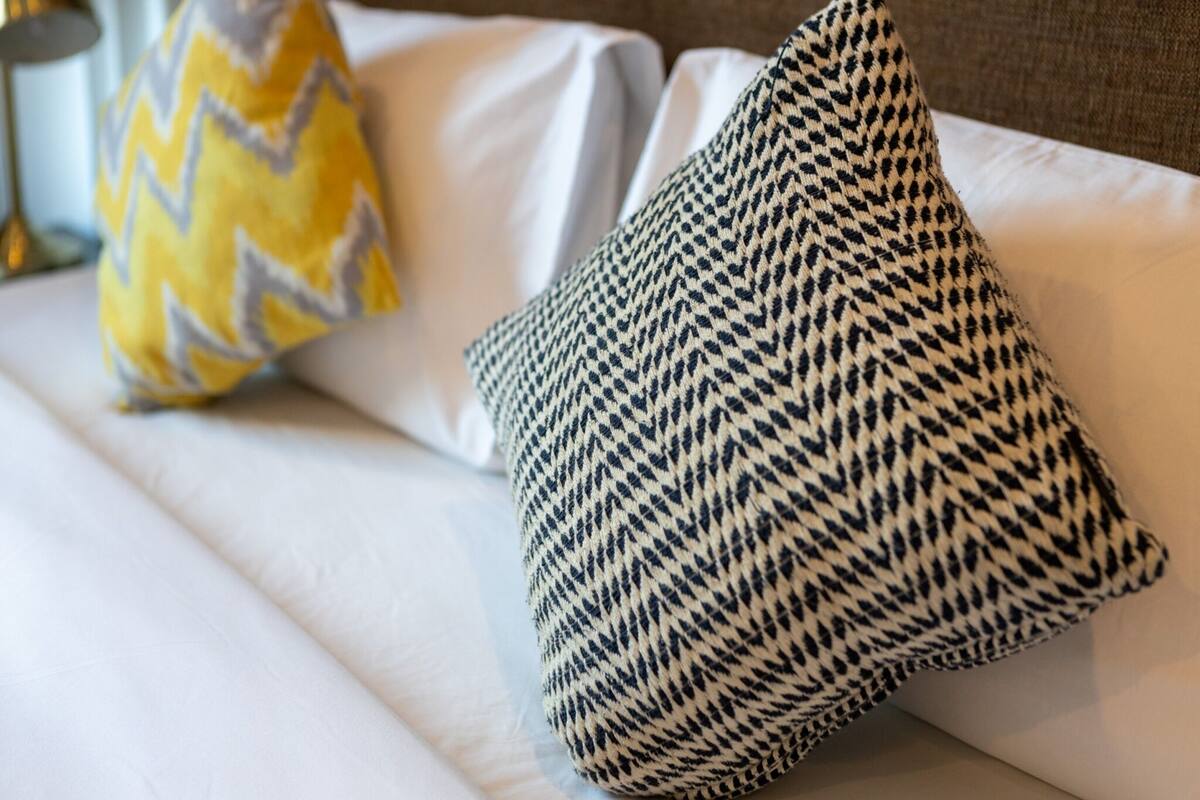 A bed with white bedding and two patterned pillows, one with a zigzag design and the other with a houndstooth pattern.