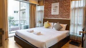 Habitación de hotel con una cama grande, una pared de ladrillo, un balcón con cortinas y un cuadro enmarcado en la pared.