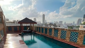 Una piscina en la azotea con cubierta de madera, un pabellón y un horizonte urbano al fondo.