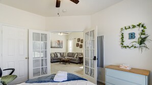 A bedroom with a bed, a dresser, and a door leading to a living area with a sofa and a coffee table.