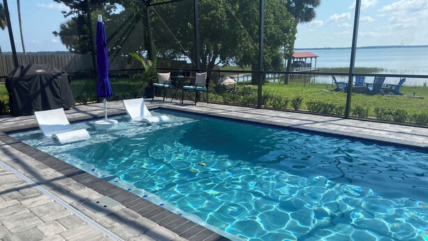 Piscina rectangular con agua cristalina, rodeada por una solana con baldosas y un área de descanso cubierta con sillas y una mesa.