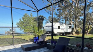 Un espacio de estar al aire libre cubierto con mobiliario de mimbre y plantas en macetas, con vistas a un lago y una caravana Kingsport.