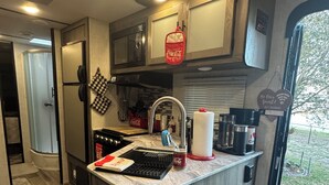 Una cocina compacta con estufa integrada, un lavamanos y una encimera con varios objetos.