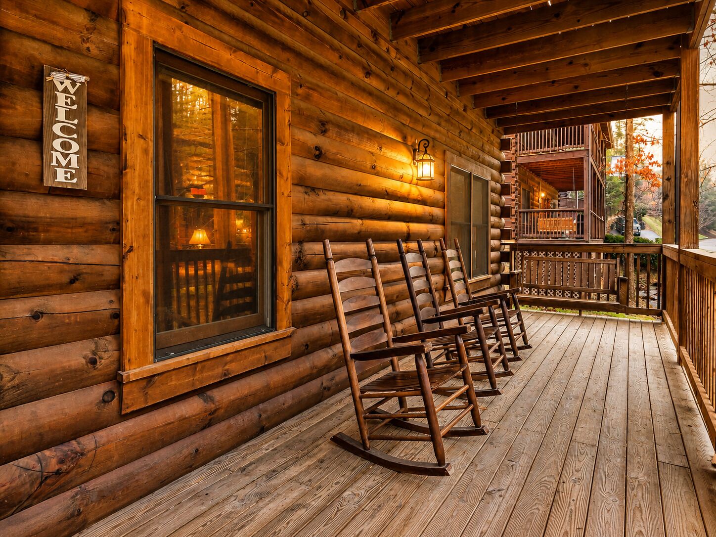 A log cabin with a wooden porch, rocking chairs, and a welcome sign.
