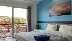 A hotel room with a bed, a painting, a nightstand, and a view of the city. - Kata Lovely Rest Bed and Breakfast (Phuket)