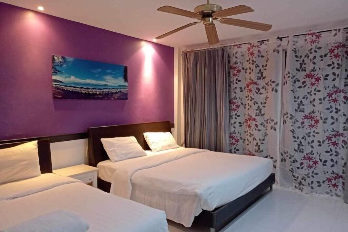 A hotel room with two beds, a ceiling fan, a painting on the wall, and floral curtains.