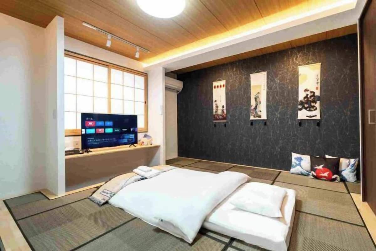 A modern hotel room with a bed, a TV, a dark wall with artwork, and a window.