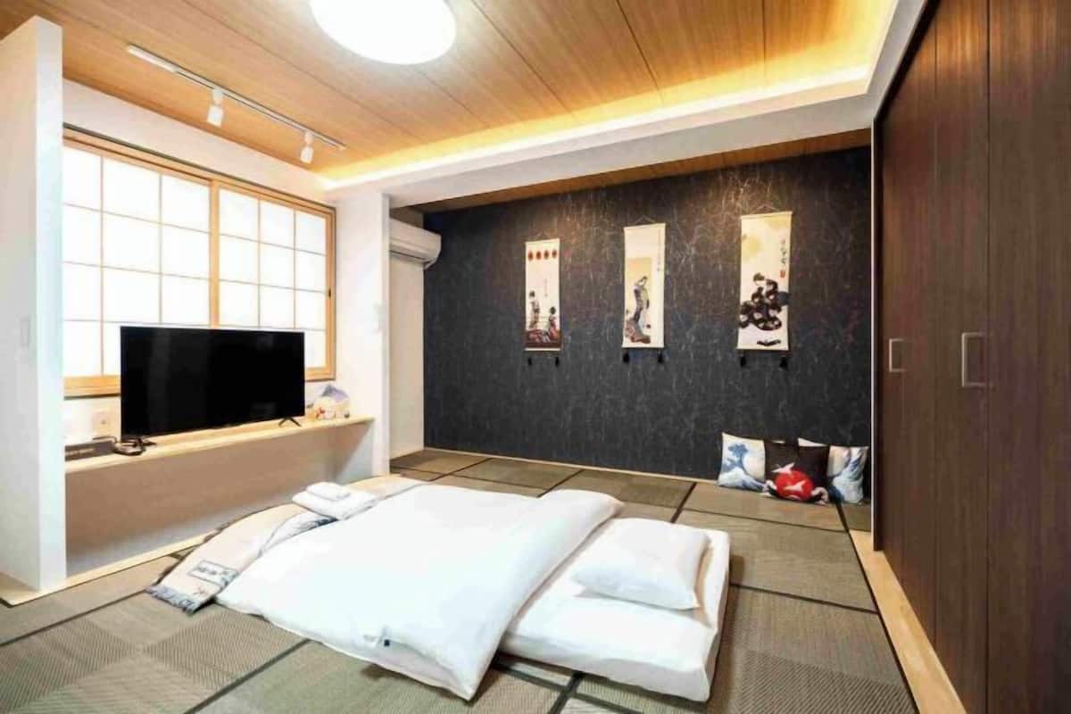 A hotel room with a bed, a television, a dark wall with artwork, and a wooden ceiling.