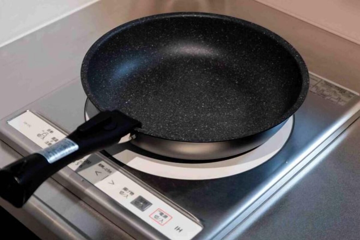 A non-stick frying pan on an induction cooktop with a digital control panel.