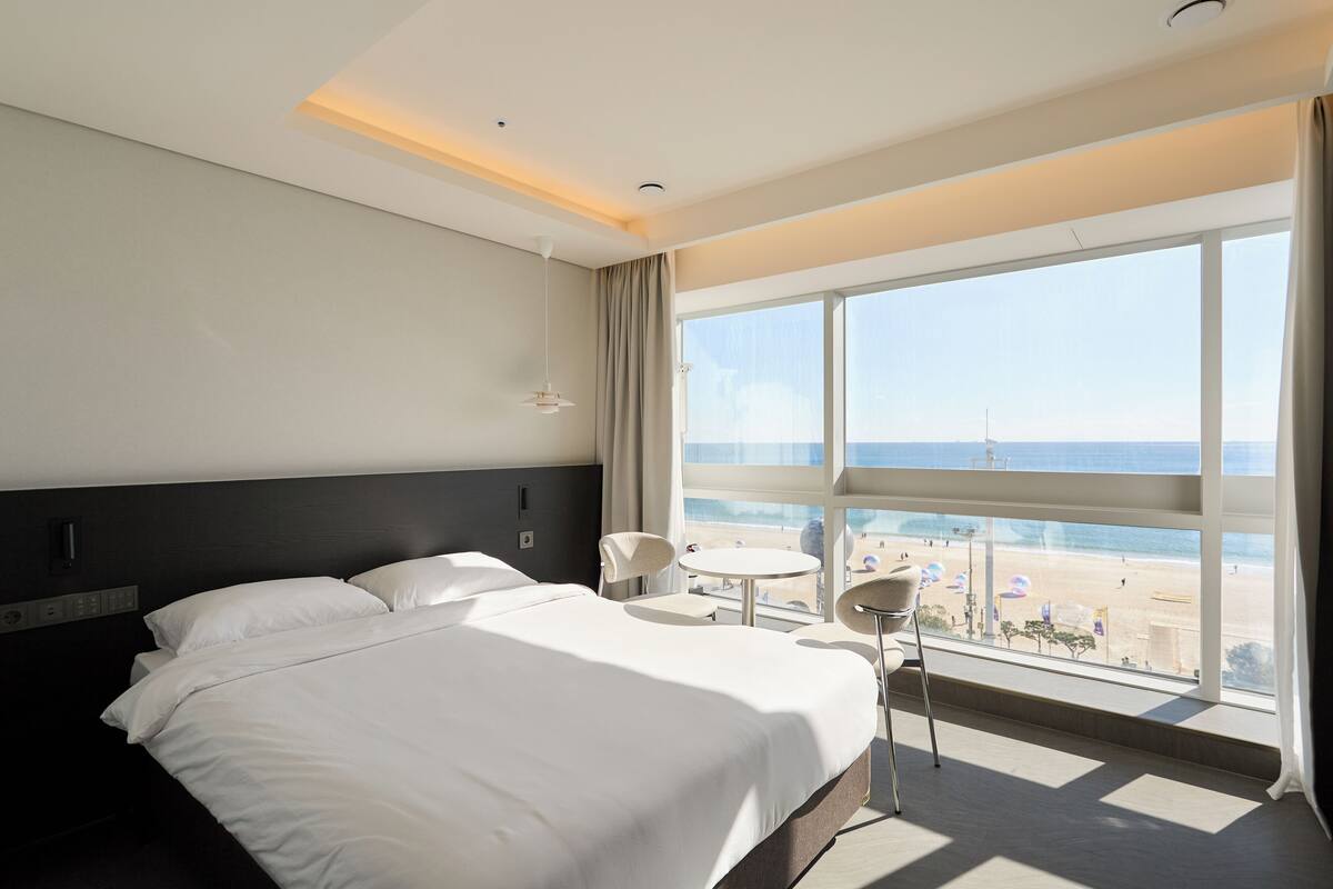 A hotel room with a large bed, a small table, and a view of the beach.