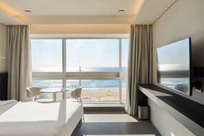 Ein Hotelzimmer mit großem Fenster, einem Bett, einem Fernseher und einem kleinen Tisch mit Stühlen.