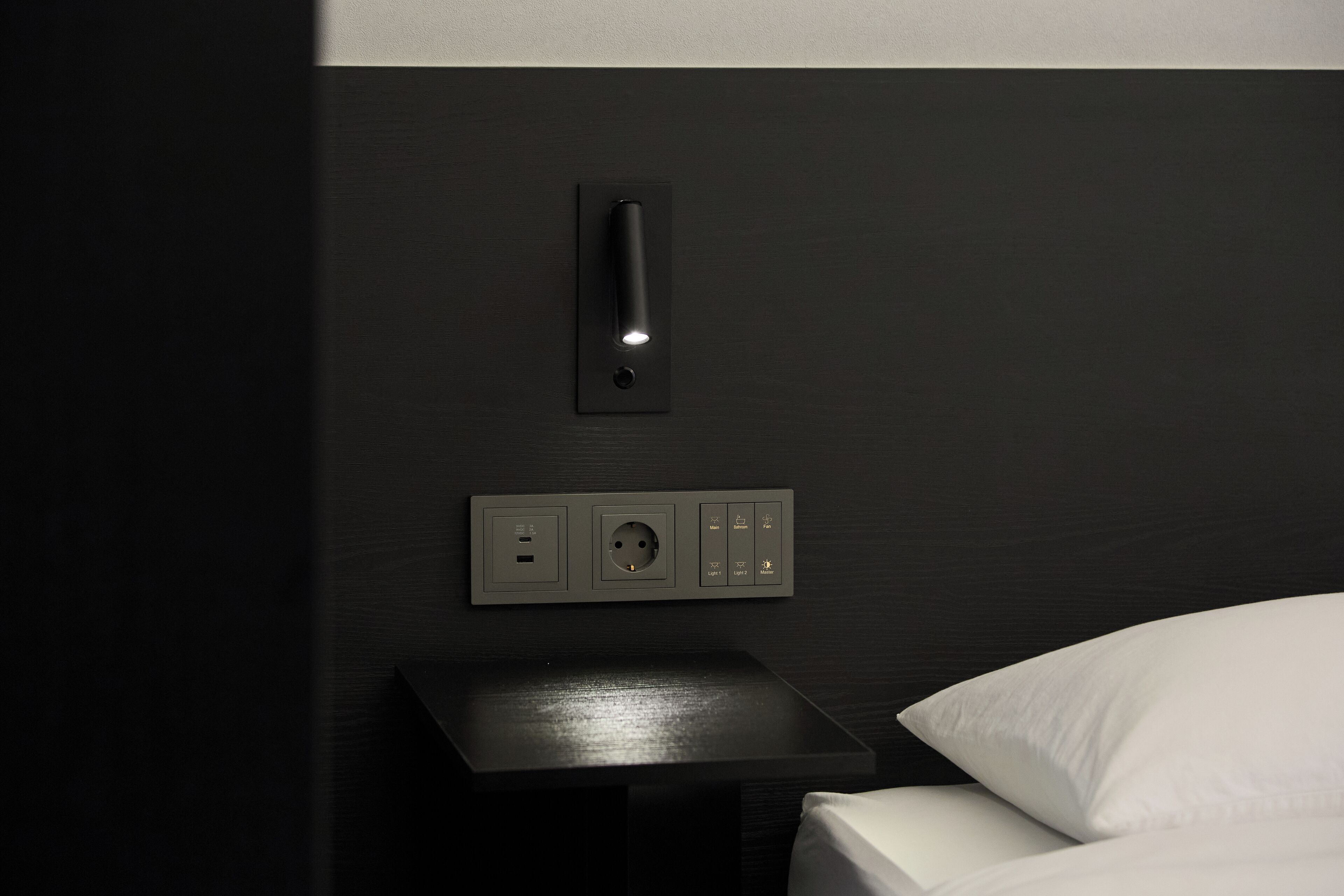 A modern bedside table with a wall-mounted power outlet and switch.