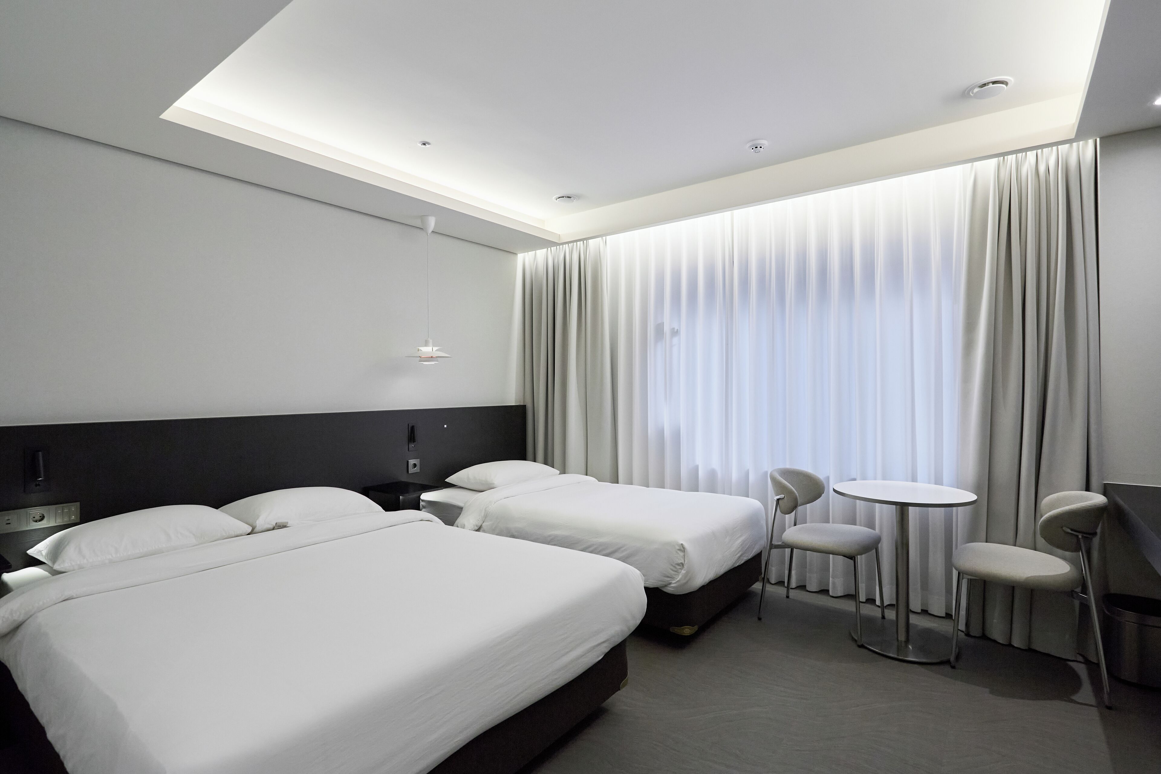 Una habitación de hotel moderna con dos camas, una mesita redonda pequeña y una silla.
