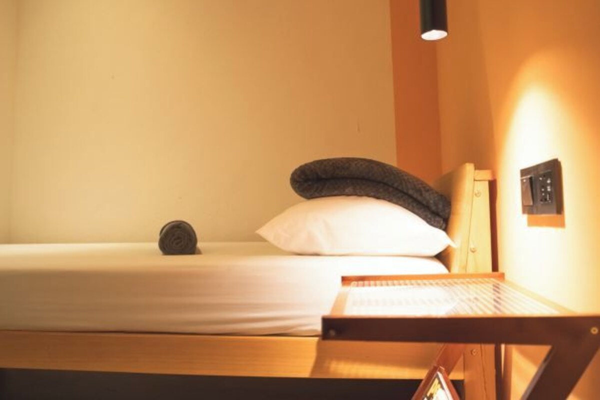 A single bed with a white sheet, a dark pillow, and a wooden headboard.