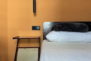 Un lit avec une tête de lit, une table de chevet et un panneau de commande fixé au mur.