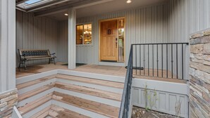A wooden porch with a bench, a door with glass panels, and a stone wall. - 4 Tan Oak - Sunriver Family Oasis, Fireplace, BBQ, Patio & Private Hot Tub (Bend)