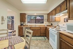 A kitchen with wooden cabinets, a built-in dishwasher, a stove, and a window overlooking a backyard. - Timber 12 - Cabin, SHARC Passes + Walkable, Private Hot Tub (Sunriver)