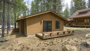 A wooden cabin with a front porch and a deck, surrounded by pine trees. - Timber 12 - Cabin, SHARC Passes + Walkable, Private Hot Tub (Sunriver)