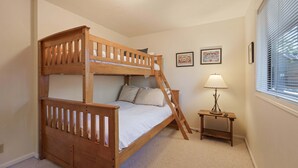 A bunk bed with a ladder, a bedside table with a lamp, and two framed pictures on the wall.