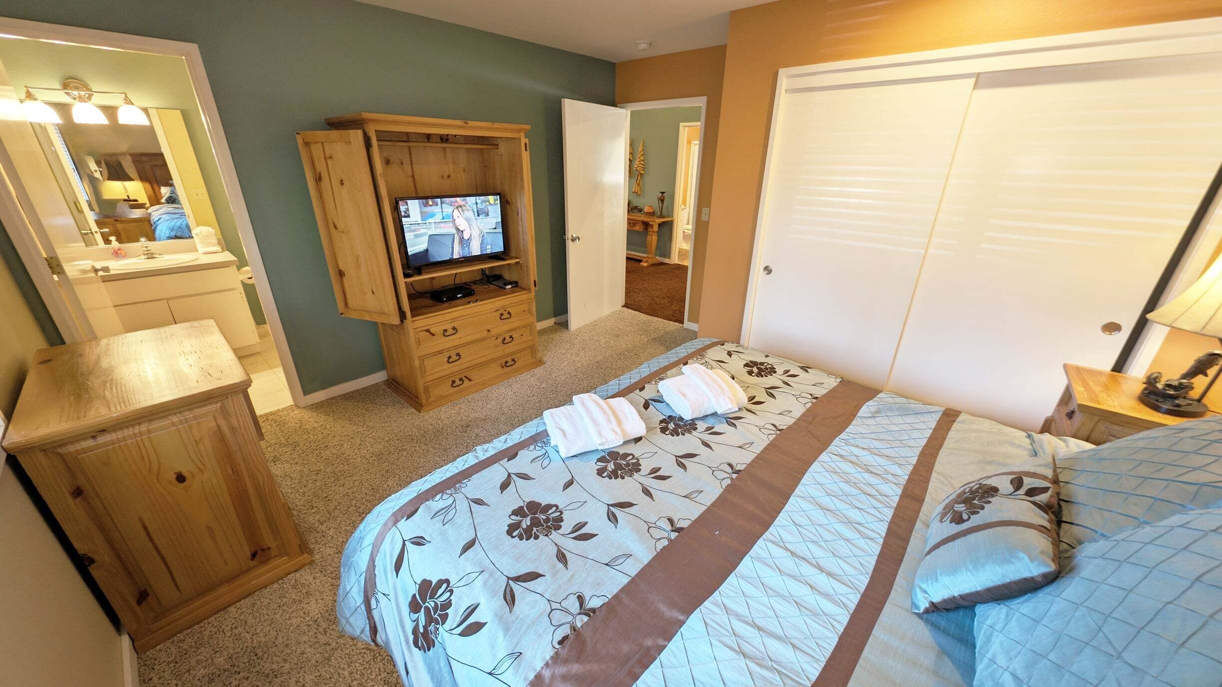 A bedroom with a bed, a wooden dresser, a television, and a closet.