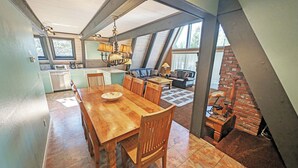 A dining area with a wooden table and chairs, a kitchen with a sink and stove, and a brick fireplace. - Trapper 11 - A-Frame, Wood Stove, Pool Table (Sunriver)