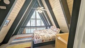 A cozy attic bedroom with a sloped ceiling, a bed with a quilt, a striped rug, and a ceiling fan. - Trapper 11 - A-Frame, Wood Stove, Pool Table (Sunriver)