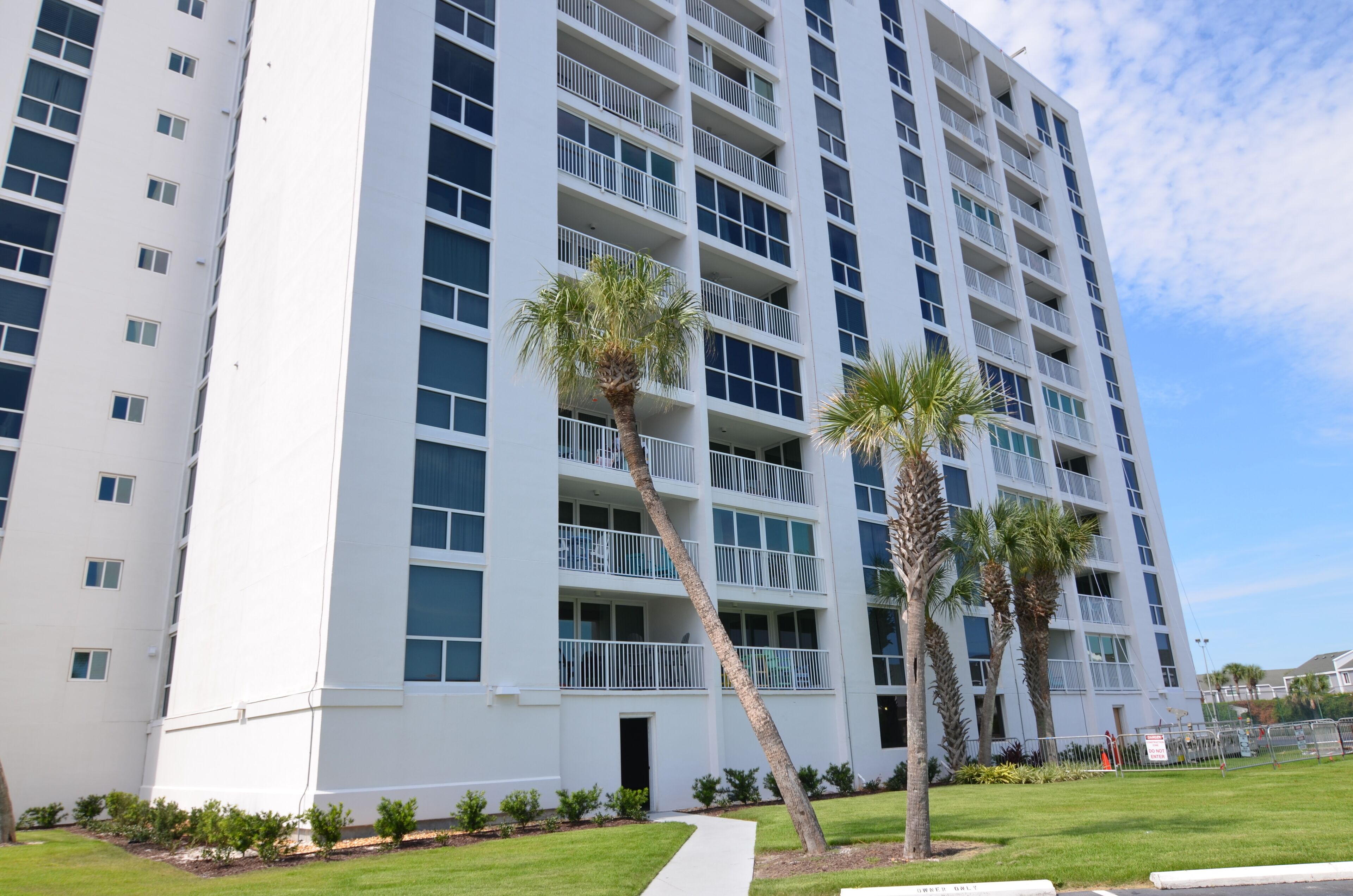 A multi-story hotel with balconies, palm trees, and a well-maintained lawn.