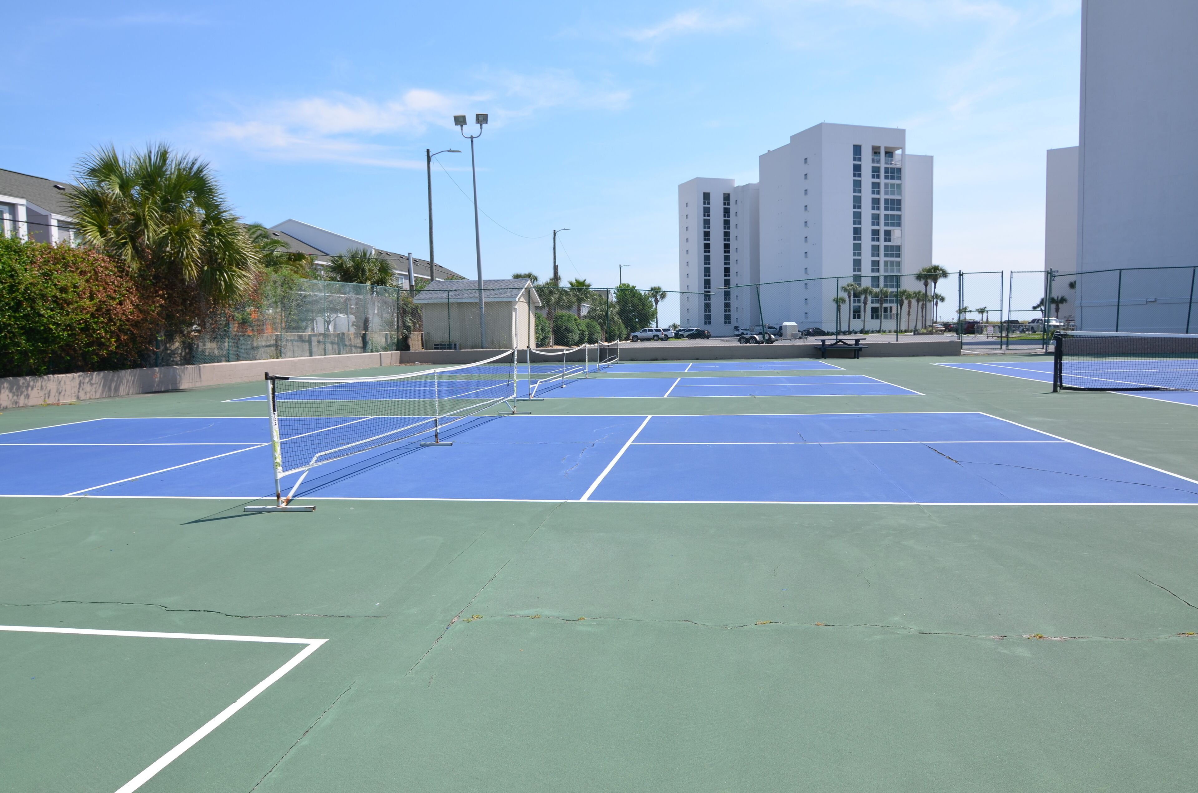 En tennisbana med nät, omgiven av ett staket, och byggnader i bakgrunden.