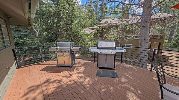 A deck with two barbecue grills, surrounded by a wooden deck and metal railing, overlooking a wooded area. - Tan Oak 15 - On Woodlands Golf Course, SHARC, Hot Tub (Sunriver)