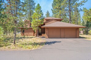 A two-story wooden cabin with a garage, surrounded by pine trees. - Tokatee 1 - Open & Bright, A/C, Hot Tub, Gas Fireplace (Sunriver)