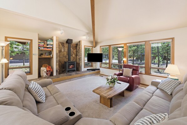 A spacious living room with a stone fireplace, comfortable seating, and large windows offering a view of the outdoors. - Tokatee 1 - Open & Bright, A/C, Hot Tub, Gas Fireplace (Sunriver)
