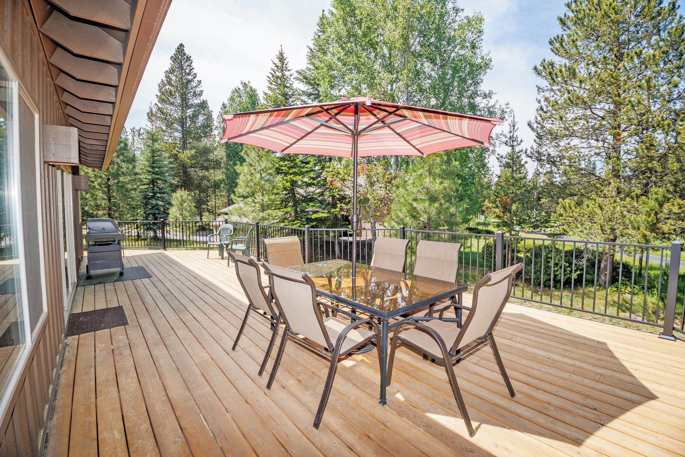A wooden deck with a glass-top table and chairs, surrounded by a metal railing.