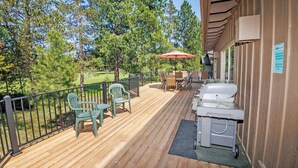 Une terrasse en bois, dotée de mobilier d’extérieur, d’un barbecue et offrant une vue sur les arbres.