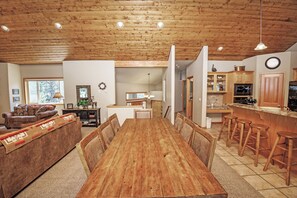 A spacious dining area with a wooden table and chairs, a kitchen with wooden cabinets, and a living area with a sofa and a lamp.
