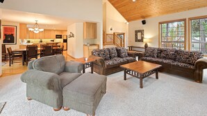 A spacious living room with a large sofa, two armchairs, and a coffee table. There is a kitchen in the background with wooden cabinets and a dining area with chairs. - Tokatee 14 - Beautiful & Spacious, SHARC, Ping Pong, A/C, Hot Tub (Sunriver)