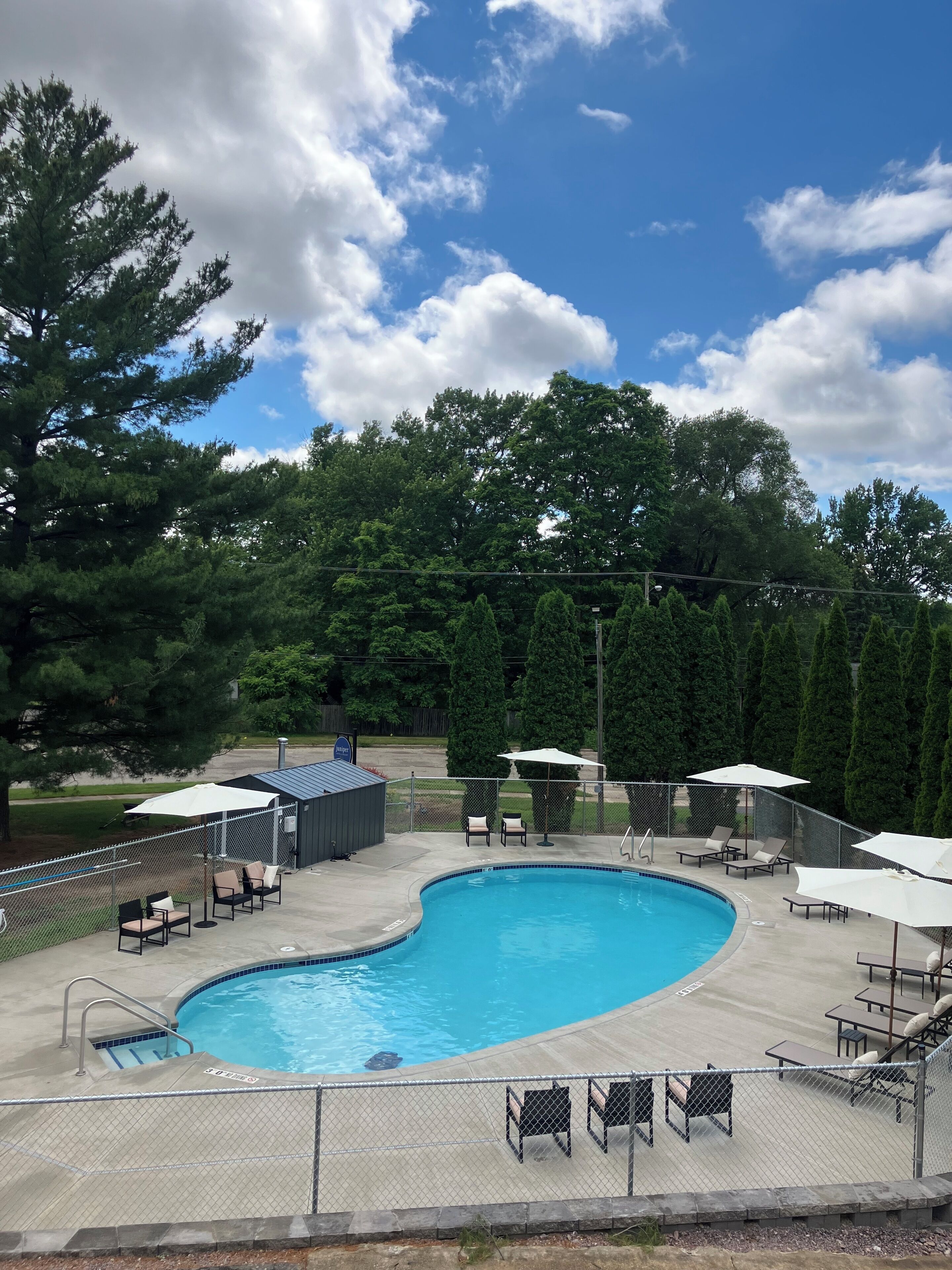 A swimming pool with a curved edge, surrounded by a deck with lounge chairs and umbrellas.