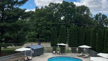 A swimming pool with a curved edge, surrounded by a deck with lounge chairs and umbrellas.