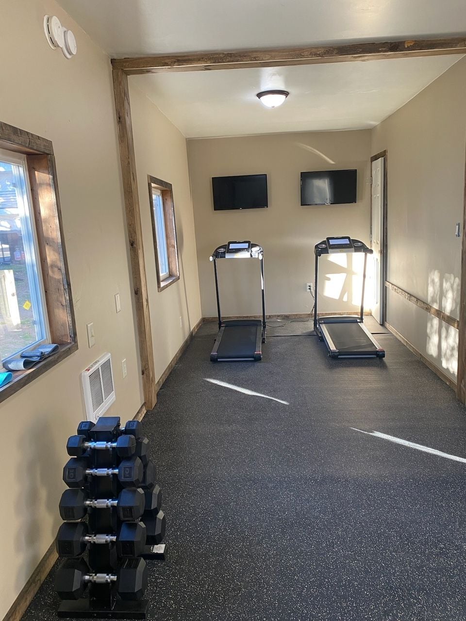 A gym with treadmills, dumbbells, and a TV on the wall.