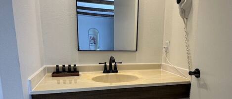 A bathroom with a sink, mirror, towel rack, and a hairdryer on the wall.