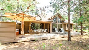 A house with a patio area featuring a table and chairs, an umbrella, and a view of the surrounding trees. - Summit View 5 - Updated Single Level, SHARC, A/C, Hot Tub (Sunriver)
